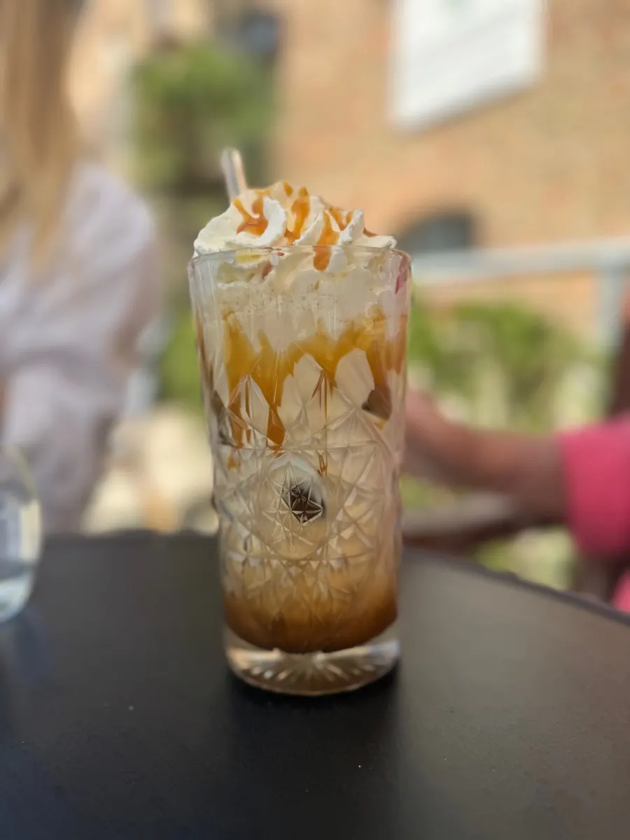Eiskaffee mit Karamell und Sahnehaube im geschliffenen Glas auf der Terrasse